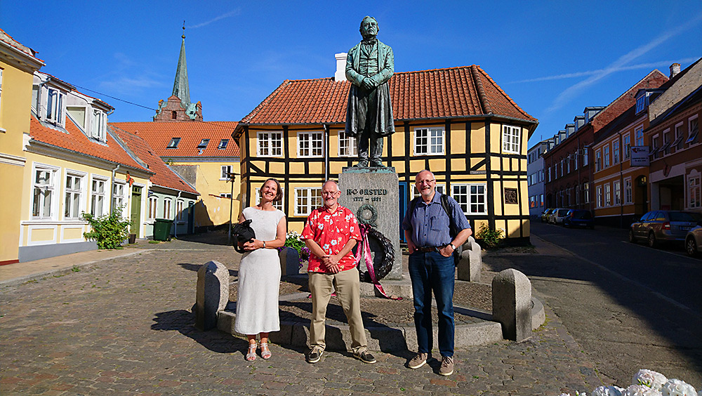 De tre Ørsted-tegneserieskabere foran statuen af H.C. Ørsted på Gaasetorvet i Rudkøbing.